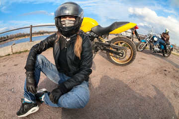 Wide angle of girl motorcycle rider sitting on earth next to bike and female biker with chopper on...