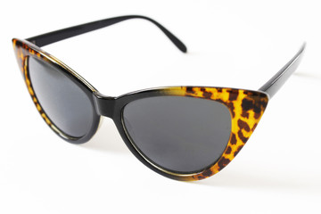 Sunglasses in the shape of cat's eye, black frame and brown leopard tips, white background.