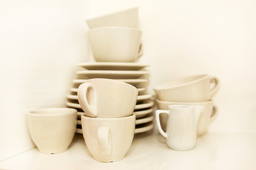 Small jug and white cups of coffee with service plate set on shelf on white background. Coffee cups with trays at the coffee bar. White crockery set. Cups, coffee, espresso and tea. Hot beverage.