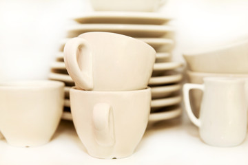 Fototapeta na wymiar Small jug and white cups of coffee with service plate set on shelf on white background. Coffee cups with trays at the coffee bar. White crockery set. Cups, coffee, espresso and tea. Hot beverage.
