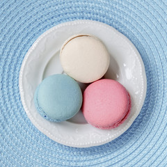 Three macaroons of different colors and different tastes in a white plate, top view. Square background