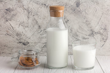 Bottle of almond milk with glass and almonds in jar on rustic white wooden table. Central view