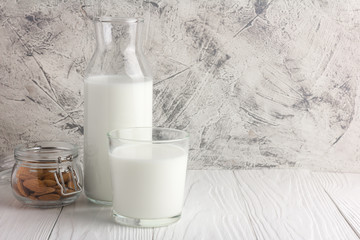 Bottle of almond milk with glass and almonds in jar on rustic white wooden table. Copy space for text and logo