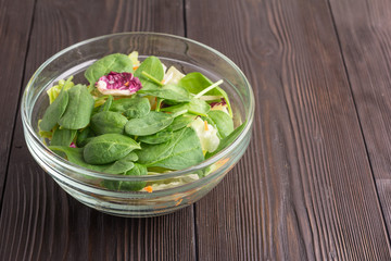 Fresh green salad with spinach, arugula, romaine and lettuce in bowl on brown wooden background