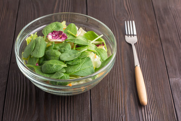 Fresh green salad with spinach, arugula, romaine and lettuce in bowl on brown wooden background