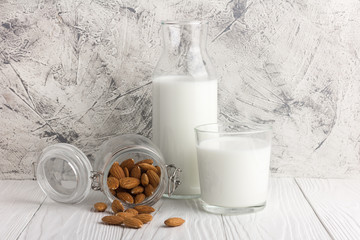 Bottle of almond milk with glass and almonds in jar on rustic white wooden table. Close-up