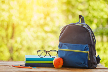 School backpack with books on wooden table and nature background