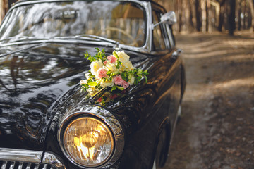 classic vintage retro black car closeup view from bumper and lamp on sunset. wedding bouquet on...