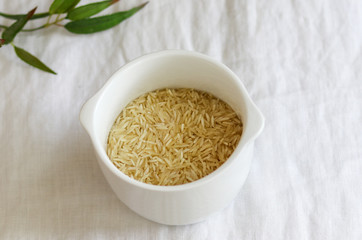 Brown jasmine wild rice in white bowl on white linen cloth and bamboo leaves on background, healthy food