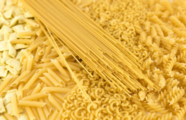 Raw pasta variety background: curls, fideuá, macaroni, pasta stuffed with meat and spaghetti