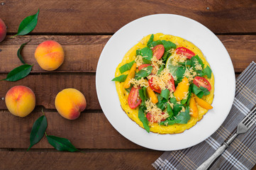 Frittata with peach, vegetables and cheese in a white plate on the rustic wooden background. Top view