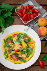 Frittata with peach, vegetables and cheese in a white plate on the rustic wooden background. Top view