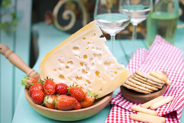 Dutch cheese with holes and strawberry. White wine in a glass. Food on the street. Veranda