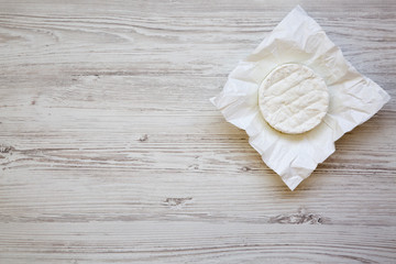 Camembert cheese on paper on white wooden background. Food for wine. From above. Top view, copy space