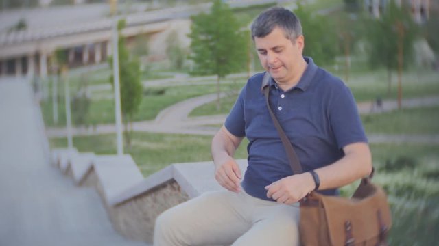 A tired middle-aged man sat down to rest after climbing stairs. A man checks on a smartphone the number of steps.