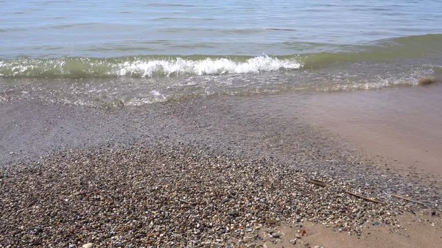 Water washing on shoreline over pebbles, rocks and beach with waves on lake on bright sunny day