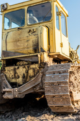 old dirty yellow crawler bulldozer, rear view, the construction machine is lit by the rays of the setting sun