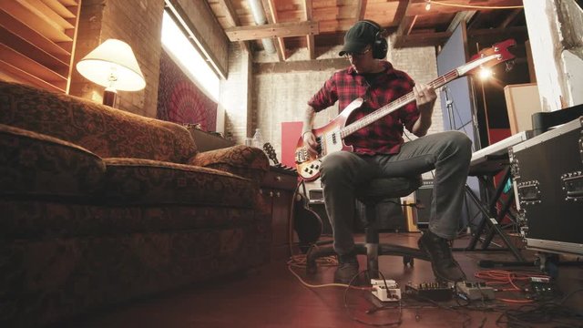 Bass Player Sitting in Recording Studio with Couch Move In. a wide angle view of a bass player sitting in a chair playing while camera moves in low angle in recording studio