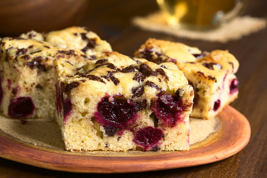 Cherry blondie or blond brownie cake baked with white and dark chocolate pieces, photographed with natural light (Selective Focus, Focus on the front of the first cake piece)