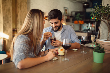 Happy couple is at the cafe where they are eating dessert and drinking wine