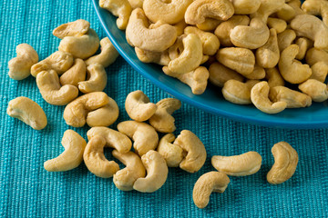 Heap of raw, organic, whole cashew nut kernels on blue plate