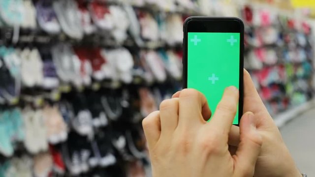 human hand holding smartphone with green screen finger pointing chromakey touchscreen scrolling flapping tapping shoes store on blurred background shopping concept internet business man closeup view