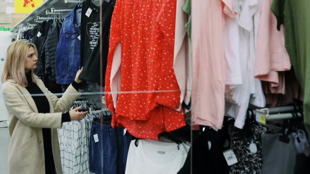 mirror reflection of young attractive blonde woman shopping trendy clothes in hypermarket holding red blouse sale sell fashion beauty shopaholic costumer attractive female shopper inside market
