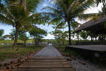 Fototapeta na wymiar Wooden path with thatched hut on tropical island