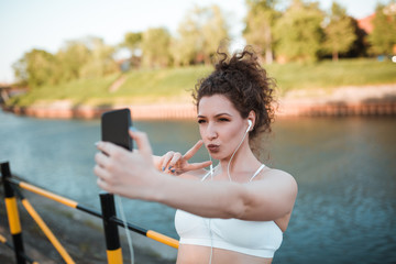 Young girl with curly hair is taking selfie during her workout by a river