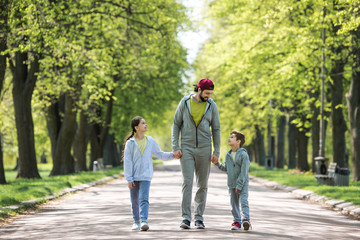 Fototapeta premium smiling father holding hands of son and daughter and walking in park