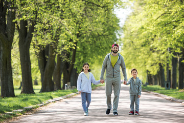 father holding hands of son and daughter and walking in park