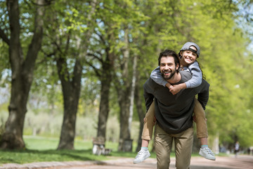 Fototapeta premium happy father doing piggyback ride to daughter in park