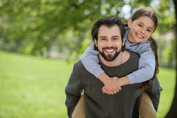 smiling father doing piggyback ride to daughter in park