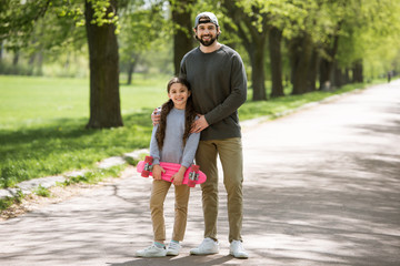 Obraz premium smiling father and daughter holding skateboard in park