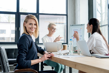 beautiful businesswoman smiling at camera while working with colleagues in office