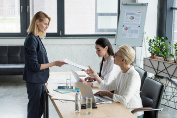 beautiful businesswoman giving documents to colleague at meeting in office