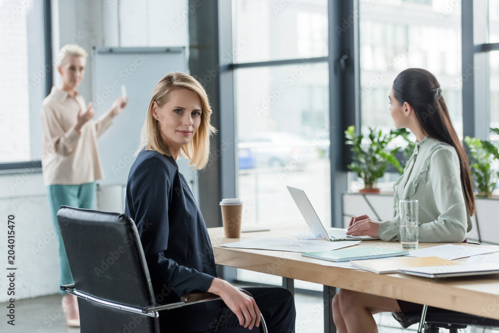 Wall mural beautiful blonde businesswoman looking at camera during meeting in office