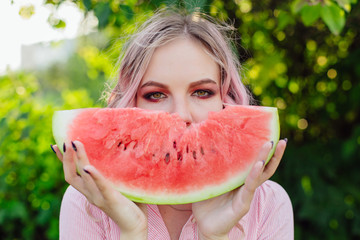 Beautiful young woman with pink hair enjoying watermelon
