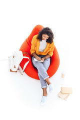 high angle view of teenage african american student girl studying while sitting on bean bag isolated on white