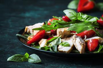 Salad with arugula, strawberries and chicken, dark background, selective focus