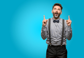 Fototapeta premium Middle age man, with beard and bow tie happy and surprised cheering expressing wow gesture pointing up