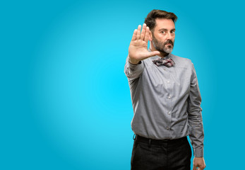 Middle age man, with beard and bow tie annoyed with bad attitude making stop sign with hand, saying no, expressing security, defense or restriction, maybe pushing