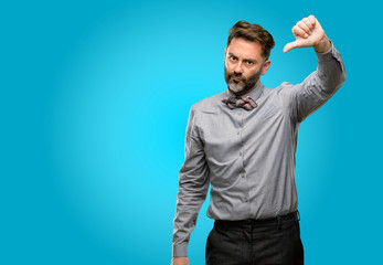 Middle age man, with beard and bow tie showing thumbs down unhappy sign of dislike, negative...