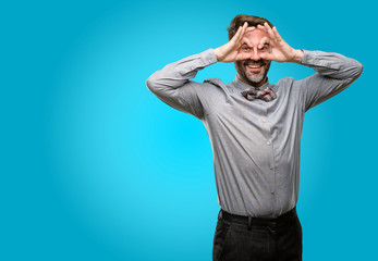 Middle age man, with beard and bow tie looking at camera through fingers in ok gesture. Imitating binoculars