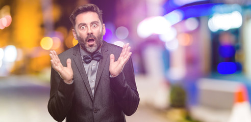 Middle age man, with beard and bow tie happy and surprised cheering expressing wow gesture at night club