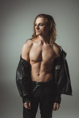 shirtless rocker with tattoo posing in black leather jacket, isolated on grey