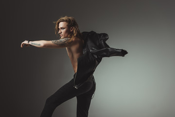 tattooed rocker man with long hair in black leather jacket, isolated on grey