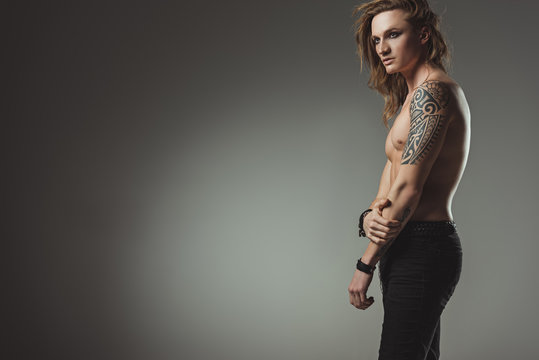 handsome shirtless man with tattoo posing in black jeans, isolated on grey with copy space