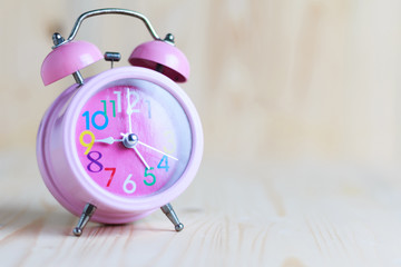 The Pink alarm clock place on the wooden table and wood background