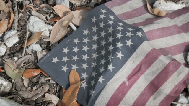 Closeup of grungy red, white and blue American flag laying on the ground covered in dirt. Neglected United States flag is symbolic of failed American values, deportation, the current political climate